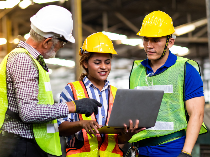 Trois professionnels portant des casques et des gilets de protection devant un ordinateur