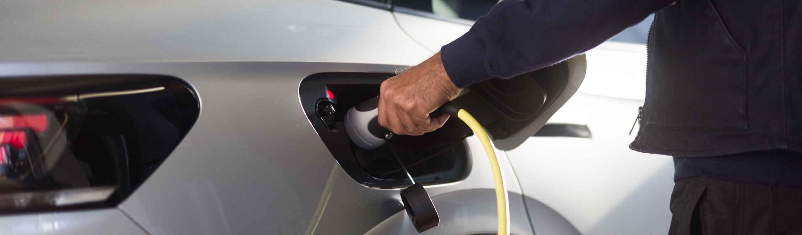 TÜV Rheinland Mitarbeiter steckt Ladekabel in E-Auto