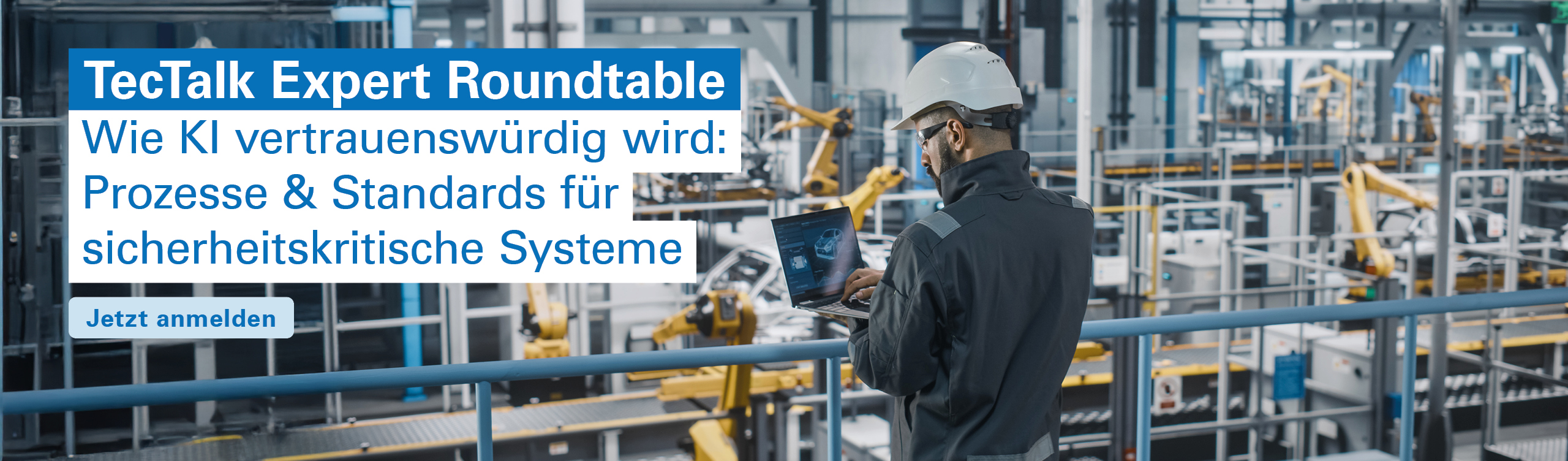 Ein Arbeiter mit Schutzhelm und Schutzkleidung steht auf einer erhöhten Plattform in einer modernen Industriehalle und bedient einen Laptop. Im Hintergrund sind mehrere gelbe Industrieroboterarme und automatisierte Produktionsanlagen zu sehen.